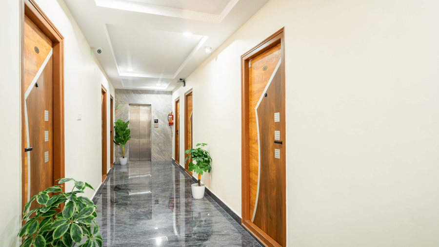 The corridor at Hotel Aurora Bliss, Gachibowli, featuring several room doors, and plants.