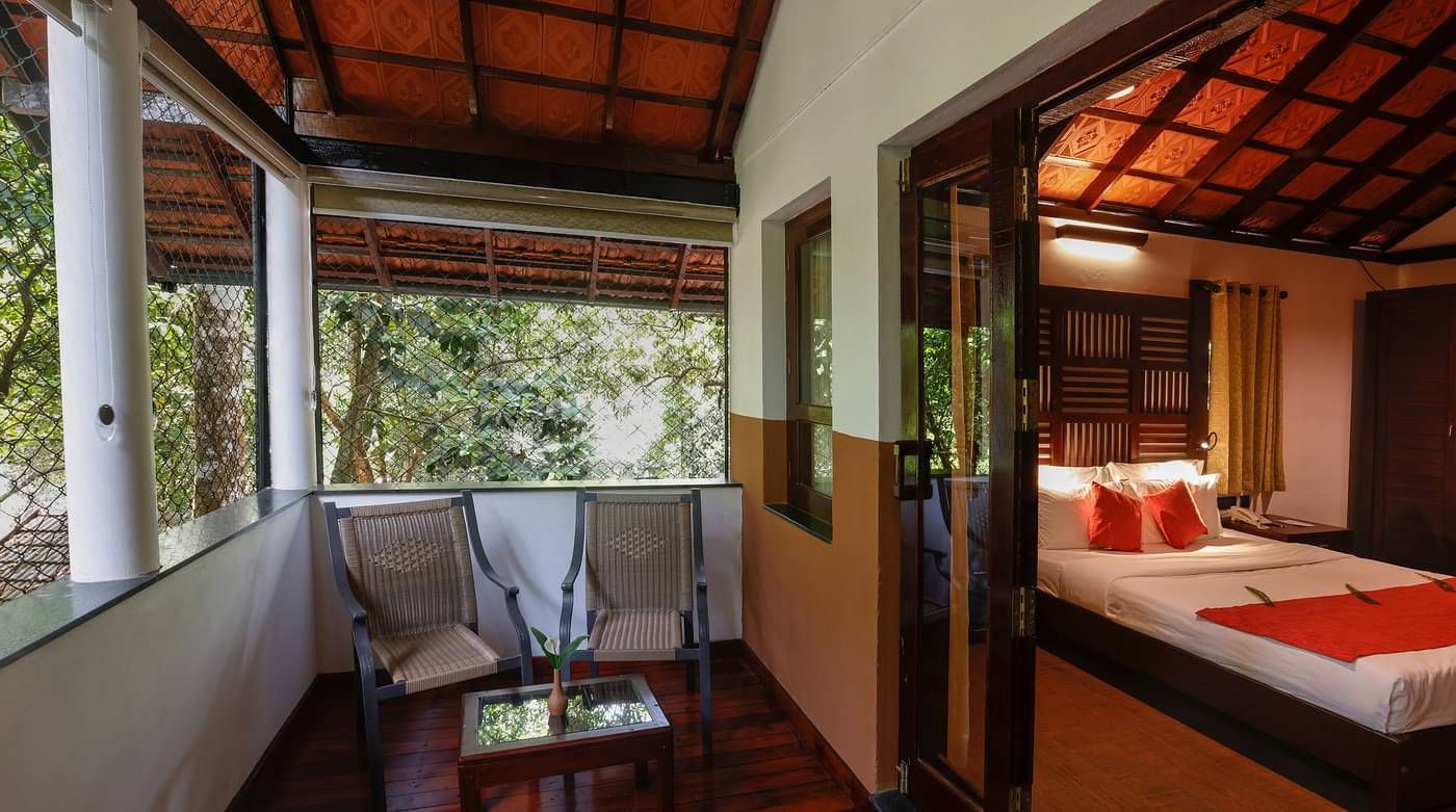 Two chairs and a coffee table in a balcony that is attached to a room | Vythiri Resort. Wayanad