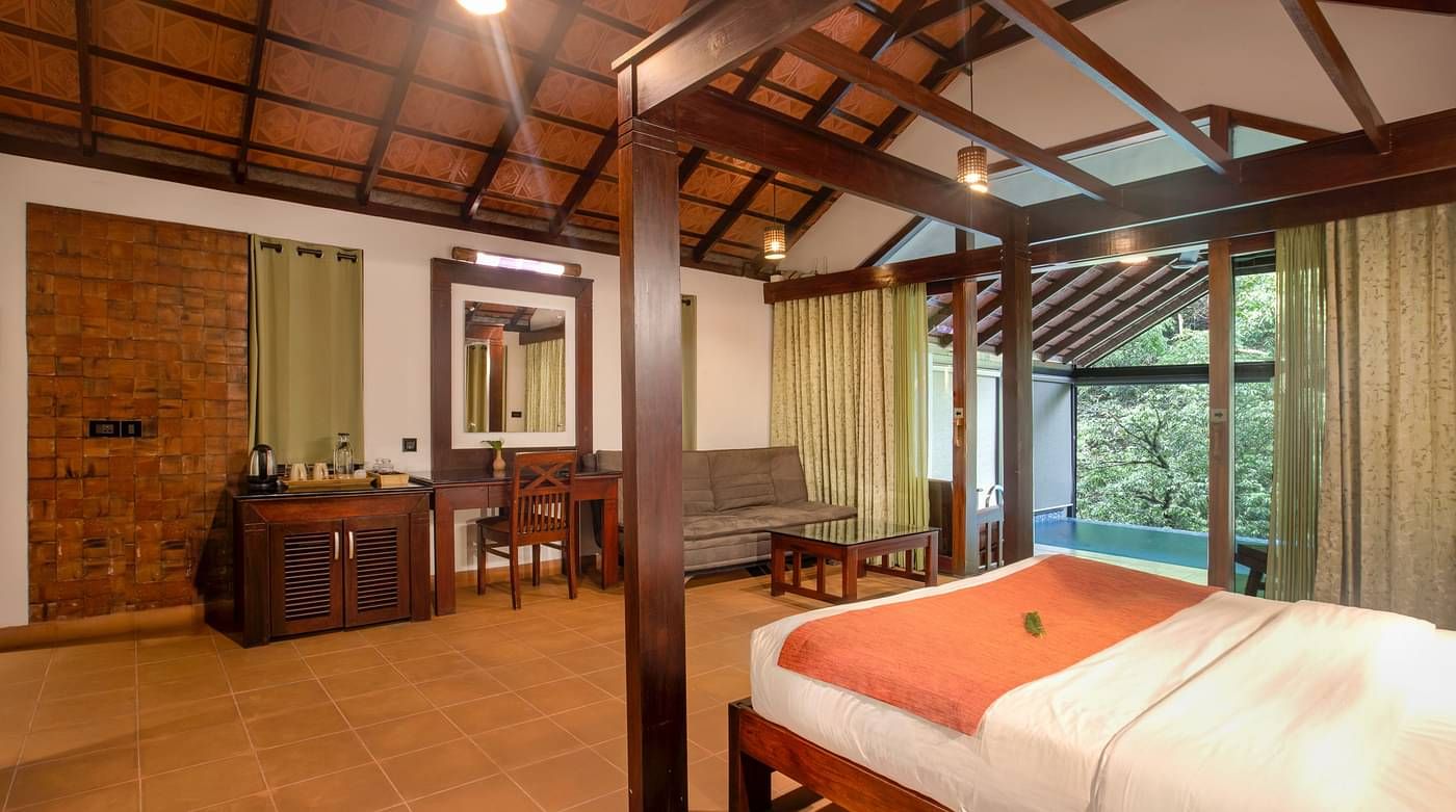 A bed in a room that has wooden furniture along with forest views | Vythiri Resort. Wayanad
