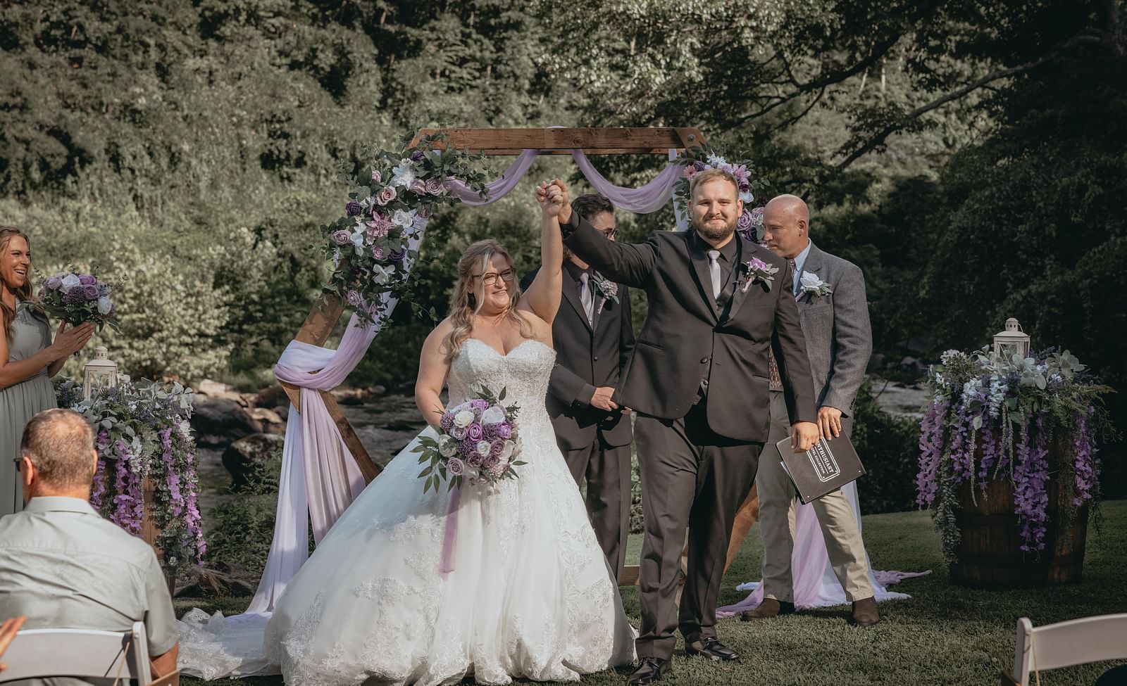 Couple celebrating their victorious wedding by waving their hands together on air at the Historic Tapoco Lodge. Other people gathered are also celebrating their wedding.