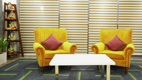 Lounge area of Lime Tree Hotels & Service Apartment Private Limited featuring yellow armchairs, a white coffee table, and a bookshelf.