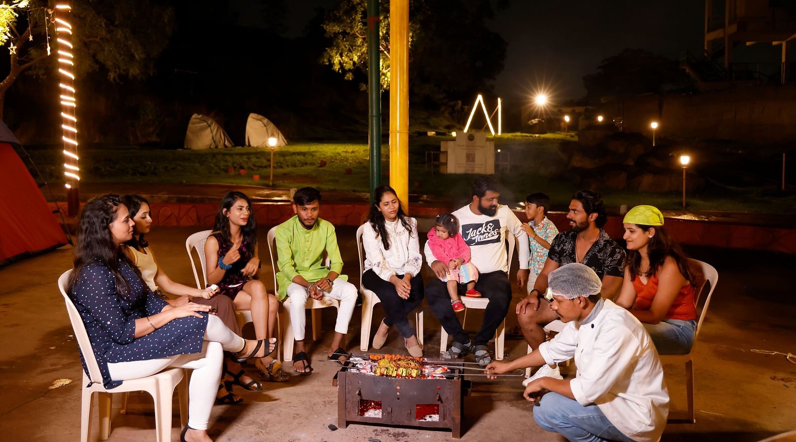 Group of friends enjoying a bonfire at a camping site in the evening | Diamond Parks, Pune