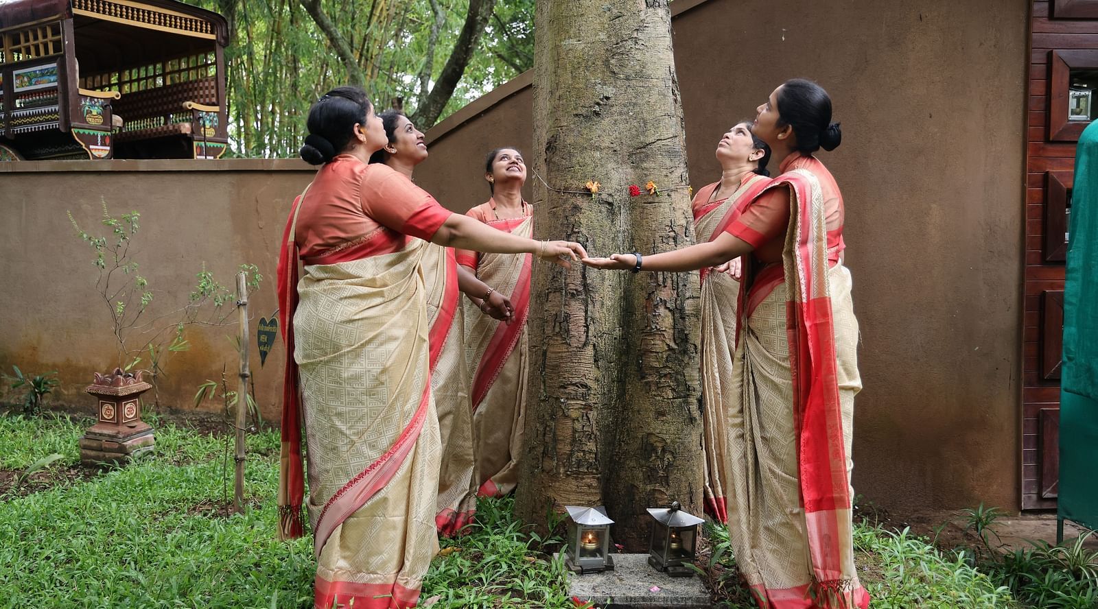 image of a group of women dressed in saree holding hands as they surround a tree at hoysala village resort in hassan