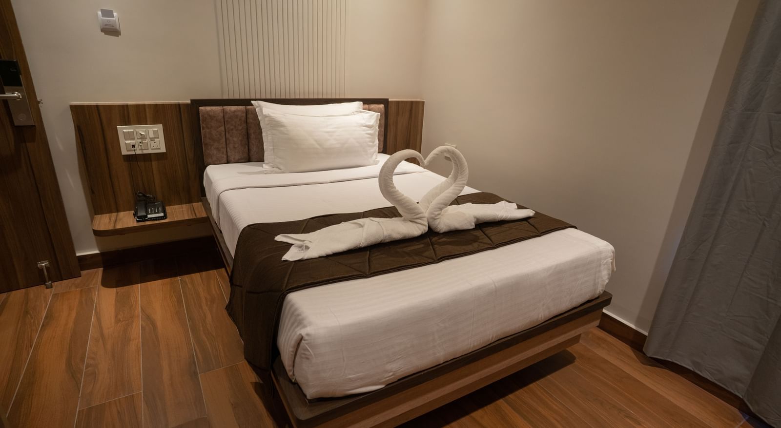 Neatly arranged single bed with towel swan decoration and bedside table at Beestay Hotels, Rajahmundry.