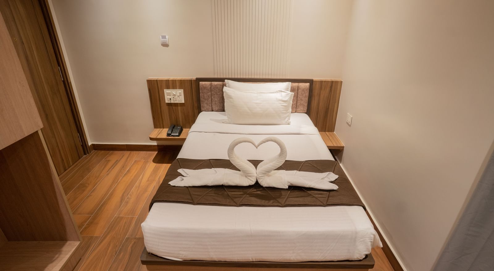 Single bed with crisp linen and towel swan decoration creating a warm ambience at Beestay Hotels, Rajahmundry.