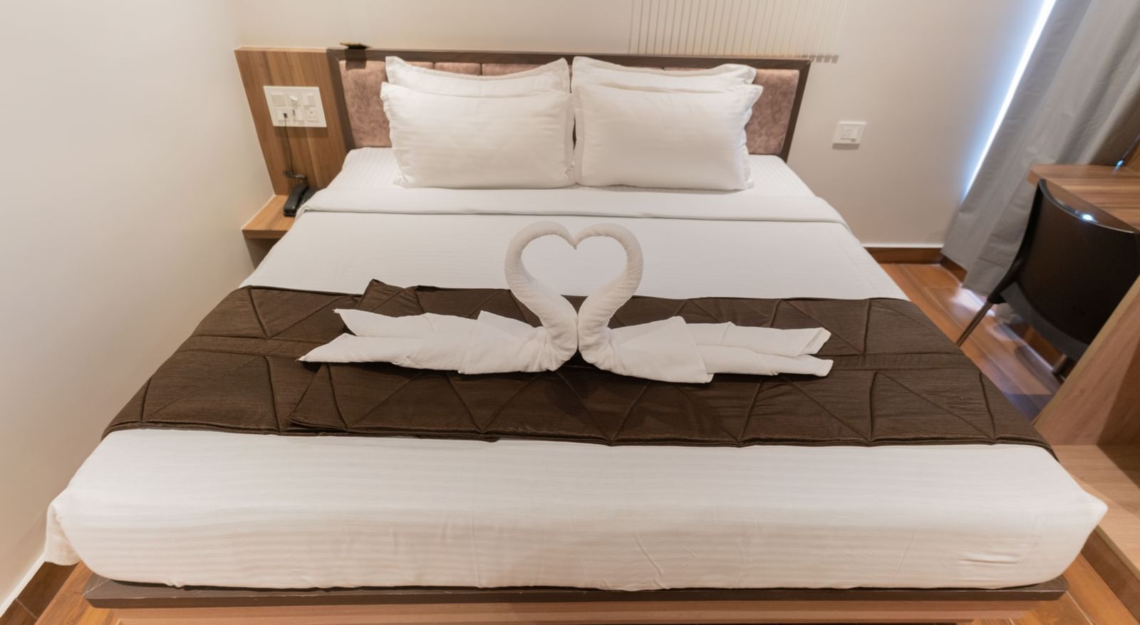 View of a spacious bed with neatly arranged swan decorations made from towels at Beestay Hotels, Rajahmundry.
