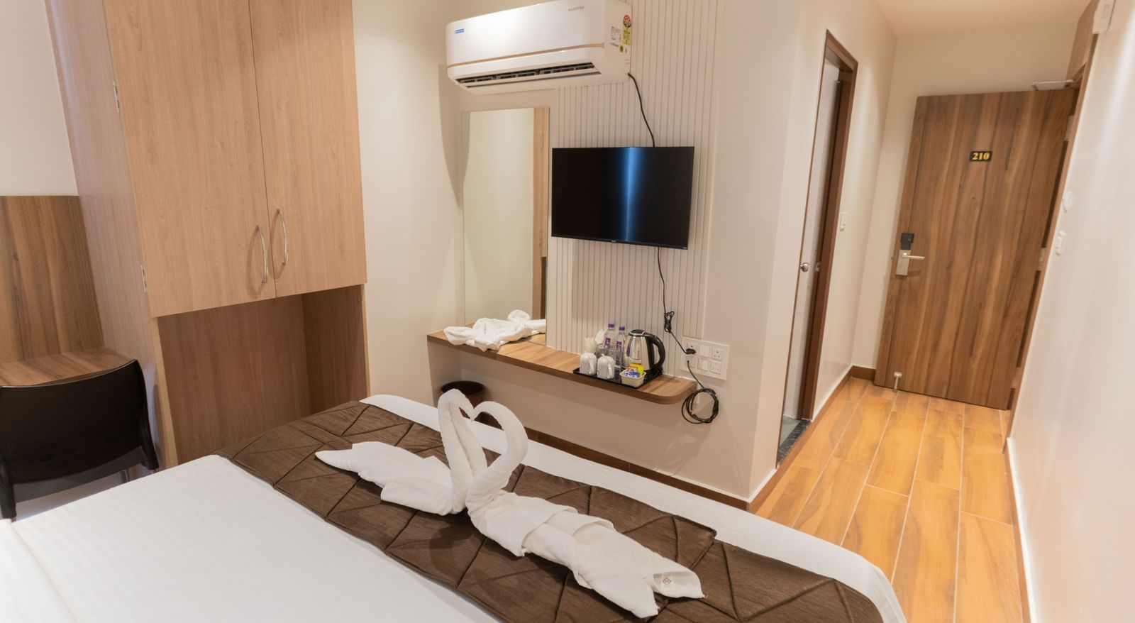 Neatly designed bedroom with wall-mounted TV and seating area beside the bed at Beestay Hotels, Rajahmundry.