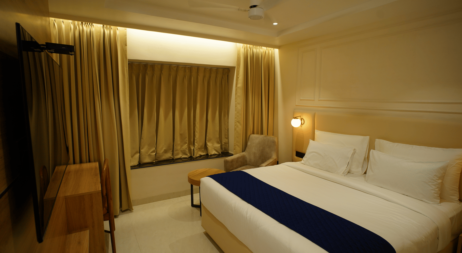  Cosy guest room at Monday Premium, Madhapur, featuring a double bed with a blue throw and a window with gold curtains.