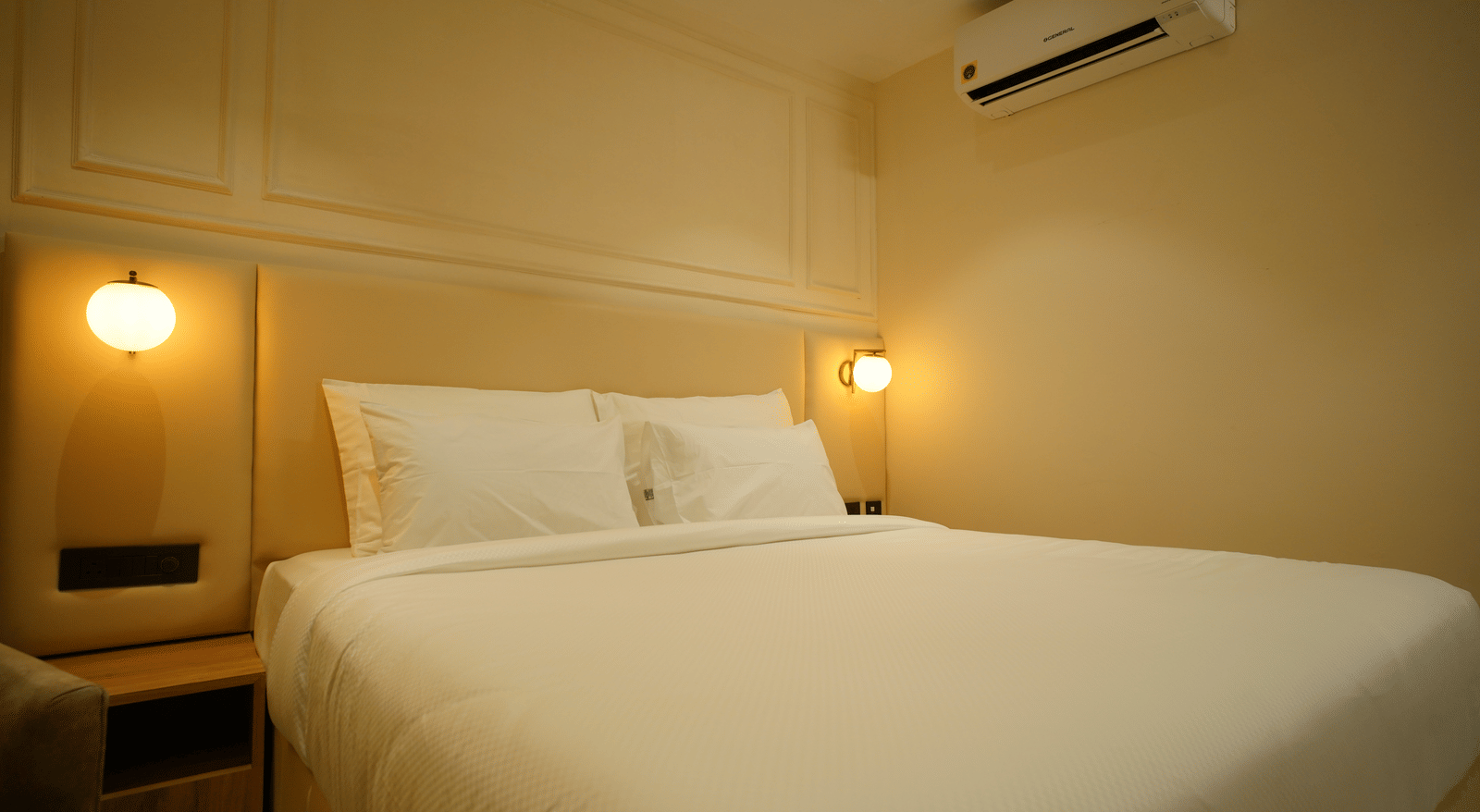  Close-up of a double bed at Monday Premium, Madhapur, showing crisp white linen, padded headboard, and warm bedside lighting.