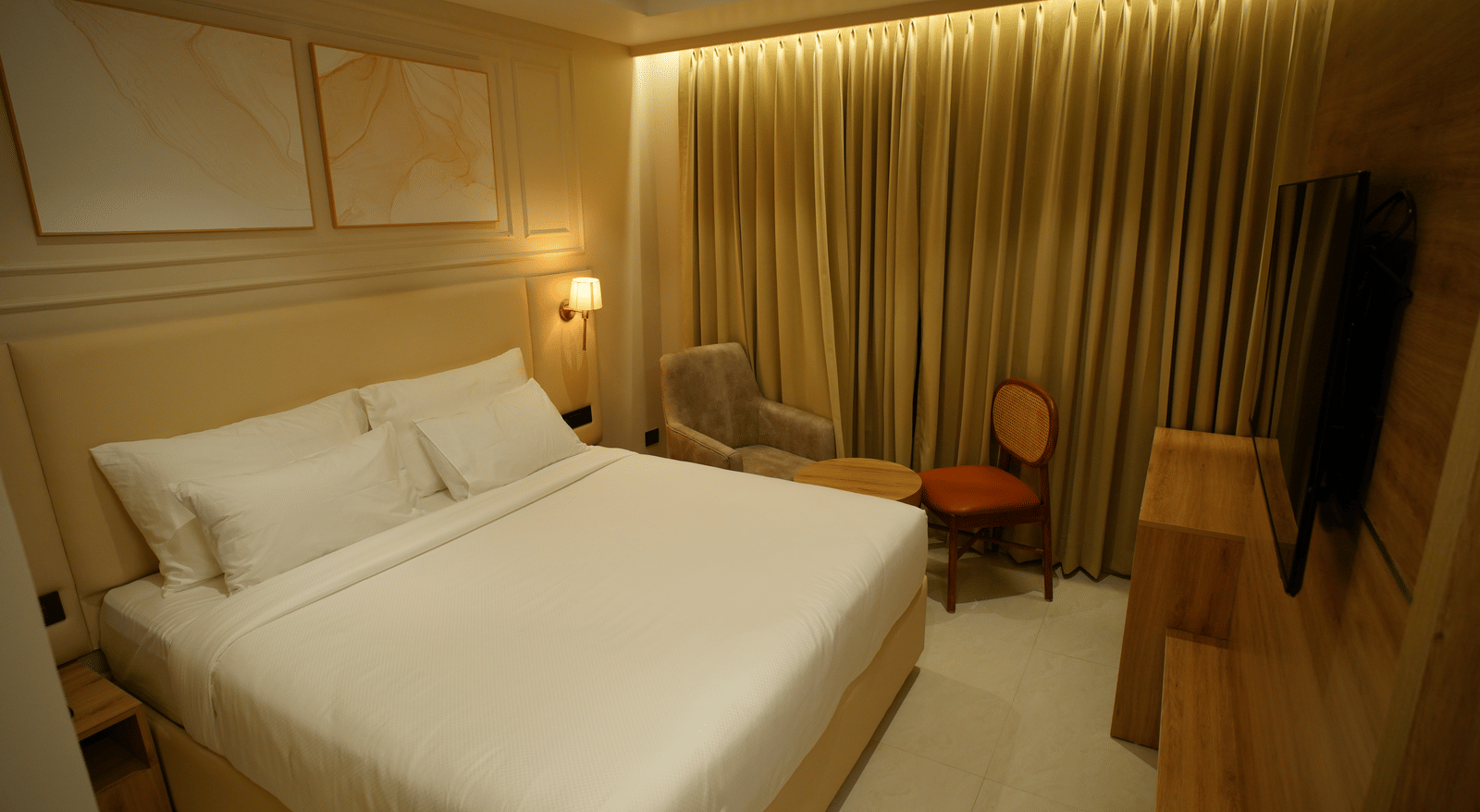  King size bed in a spacious guest room at Monday Premium, Madhapur, featuring framed artwork and gold, draped curtains. 