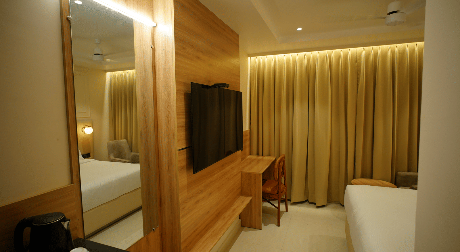  Well-designed guest room at Monday Premium, Madhapur, featuring a wood-panelled TV wall, mirrored section, and full-length gold curtains.