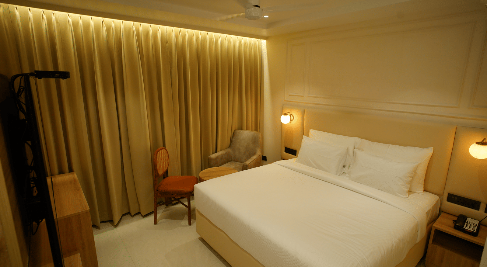 Elegant double room at Monday Premium, Madhapur, featuring a large bed, gold curtains, and a seating area with a small table.