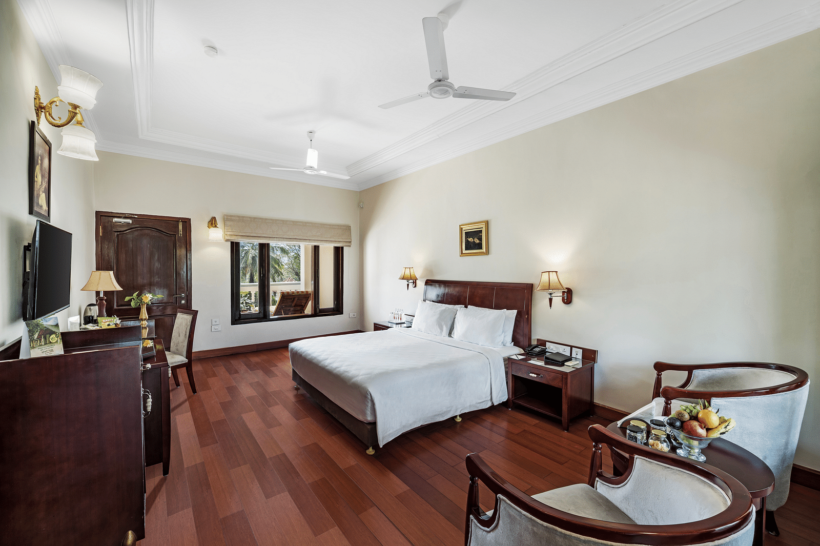 An image of the Garden room with river view featuring a queen size bed, bed side tables, lamps, ceiling fan, flat screen TV, and chairs - GReaT Trails River View Resort Thanjavur By GRT Hotels