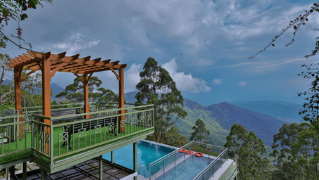 Balcony with a view of the ground-floor swimming pool, surrounded by trees and hills - Fragrant Nature Munnar