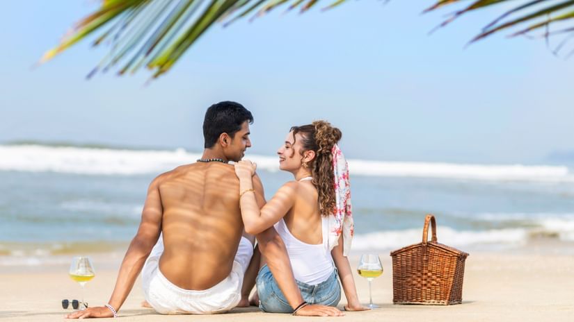 Couple enjoying a romantic beach picnic on the sand with the sea in the background.
