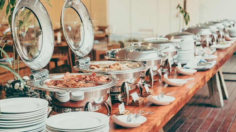 Elegant buffet setup with a variety of hot dishes in stainless steel chafing dishes, neatly arranged on a wooden table with plates and cutlery.