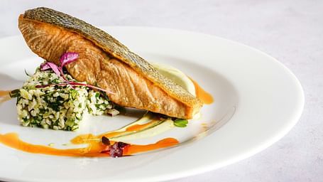 Cooked salmon served in a plate with chopped garlic and coriander leaves