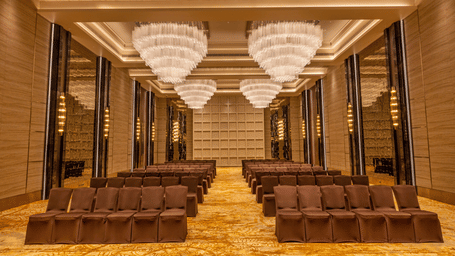 A banquet hall with theatre-style seating arrangement and majestic chandeliers at Grand Madurai by GRT Hotels.