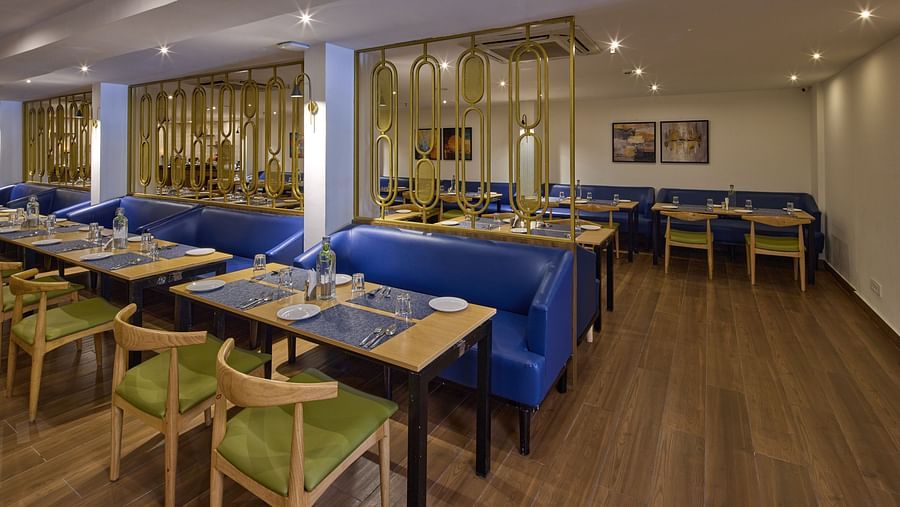 A dining area with wooden floors, glass tables, upholstered chairs in green and blue cushions, all lit by ambient lighting - Grand Continent, Brookefield