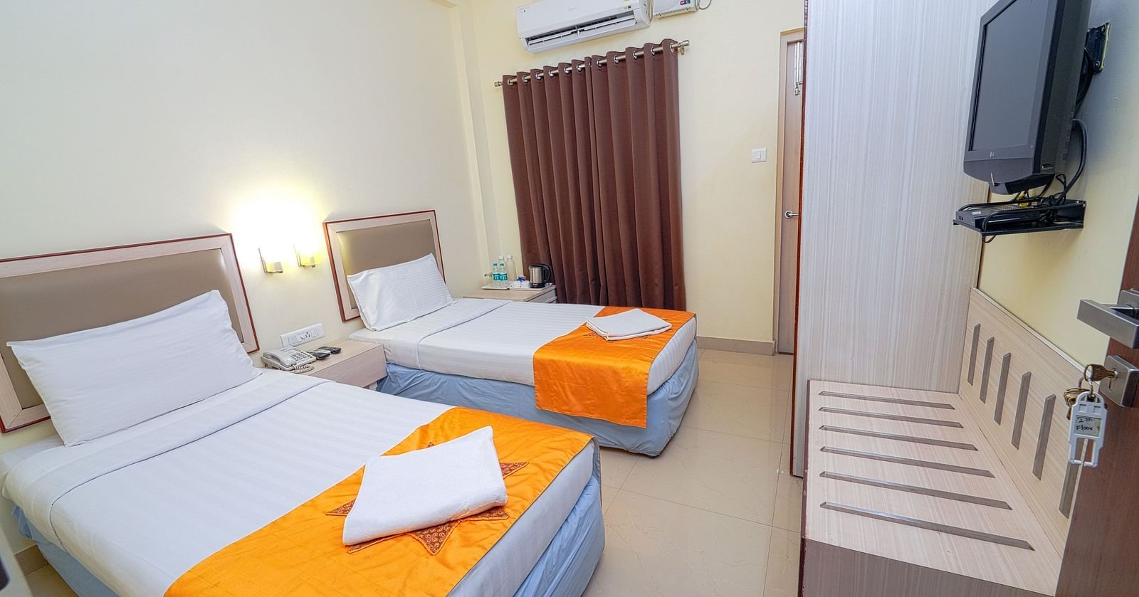 A twin bedroom with light blue bedding, air conditioning, and a wall-mounted TV at Greens Inn - Cozy Accommodations in Ramoji Film City.