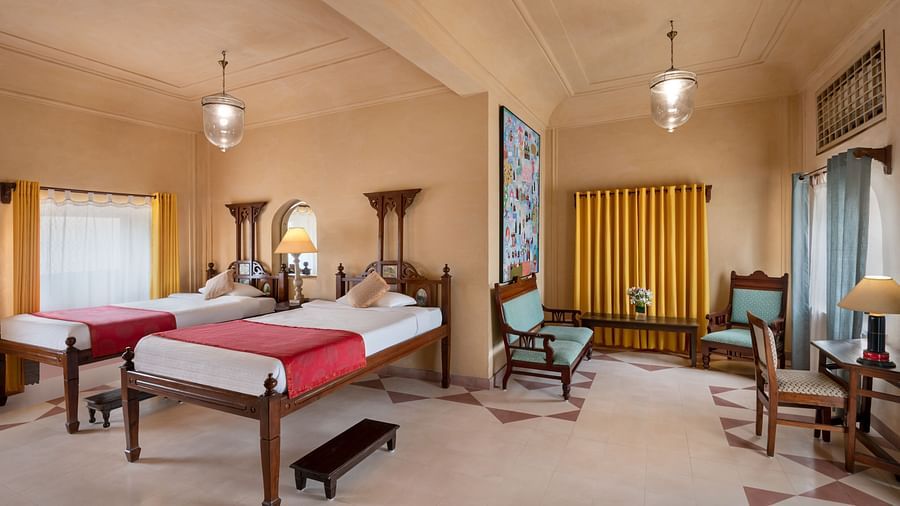 A room with two single beds, chairs, a desk, and a small bench in Tijara Fort-Palace - 19th Century, Alwar.