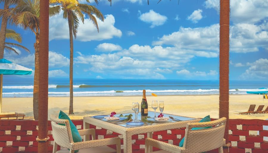 chairs and a table inside a shack with blue sky and the sea in view - Caravela Beach Resort Goa