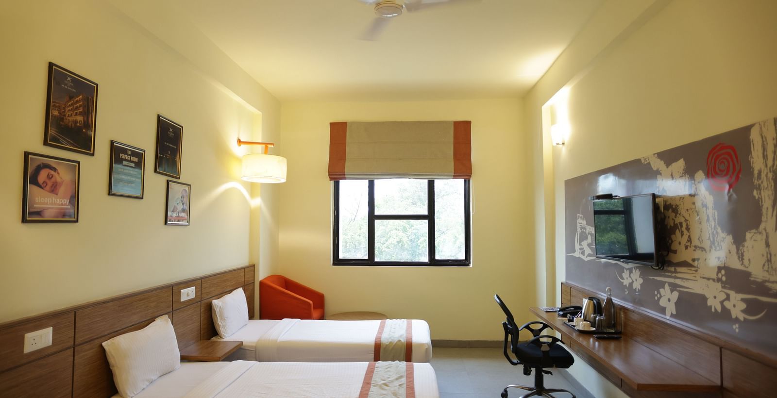 full view image of a room featuring the single beds placed opposite the television along with a window and a cushioned armchair in the far end - Max Hotel Jabalpur
