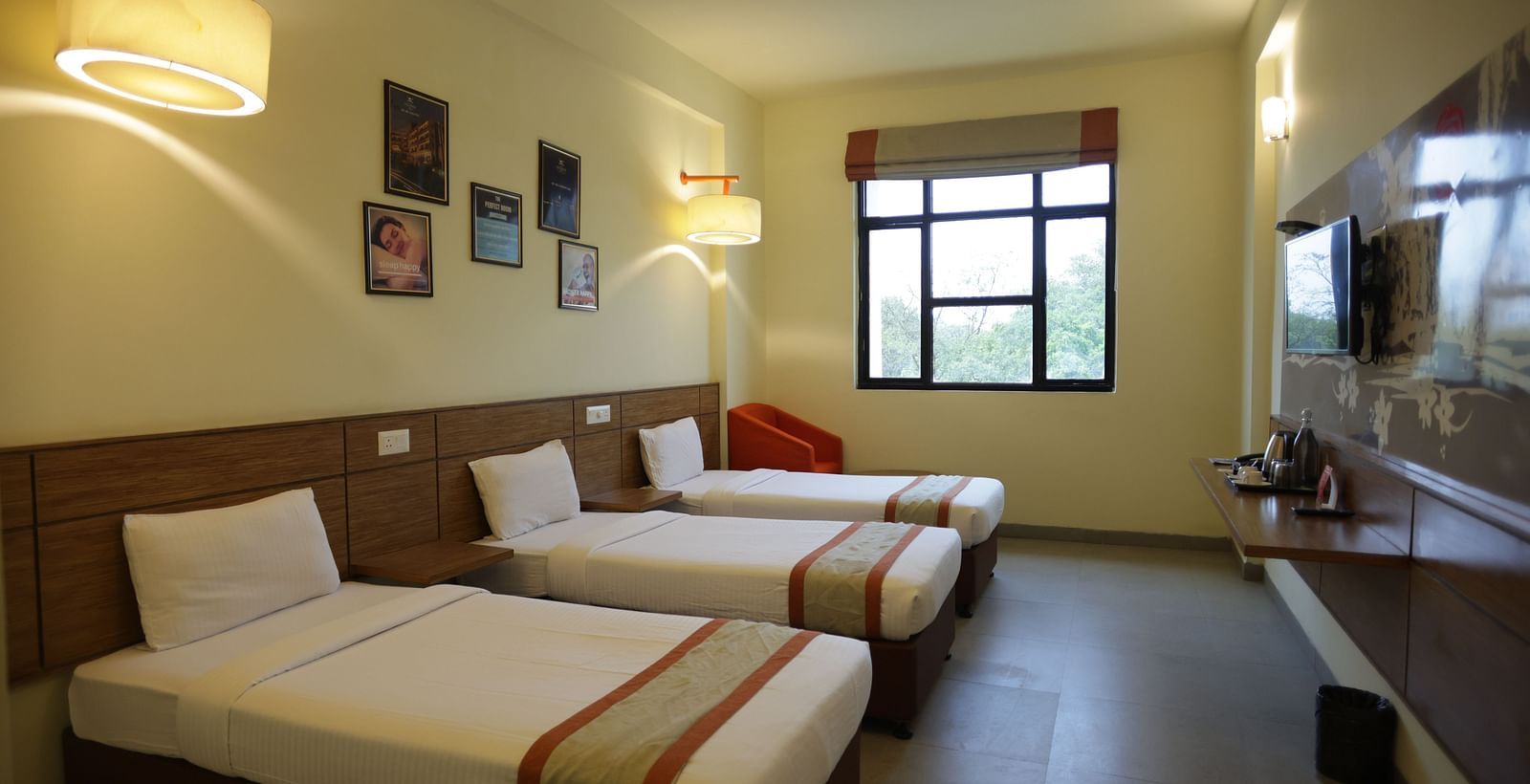 a neatly kept room with three comfortable single beds with small photo frames hung on the wall behind them - Max Hotel Jabalpur