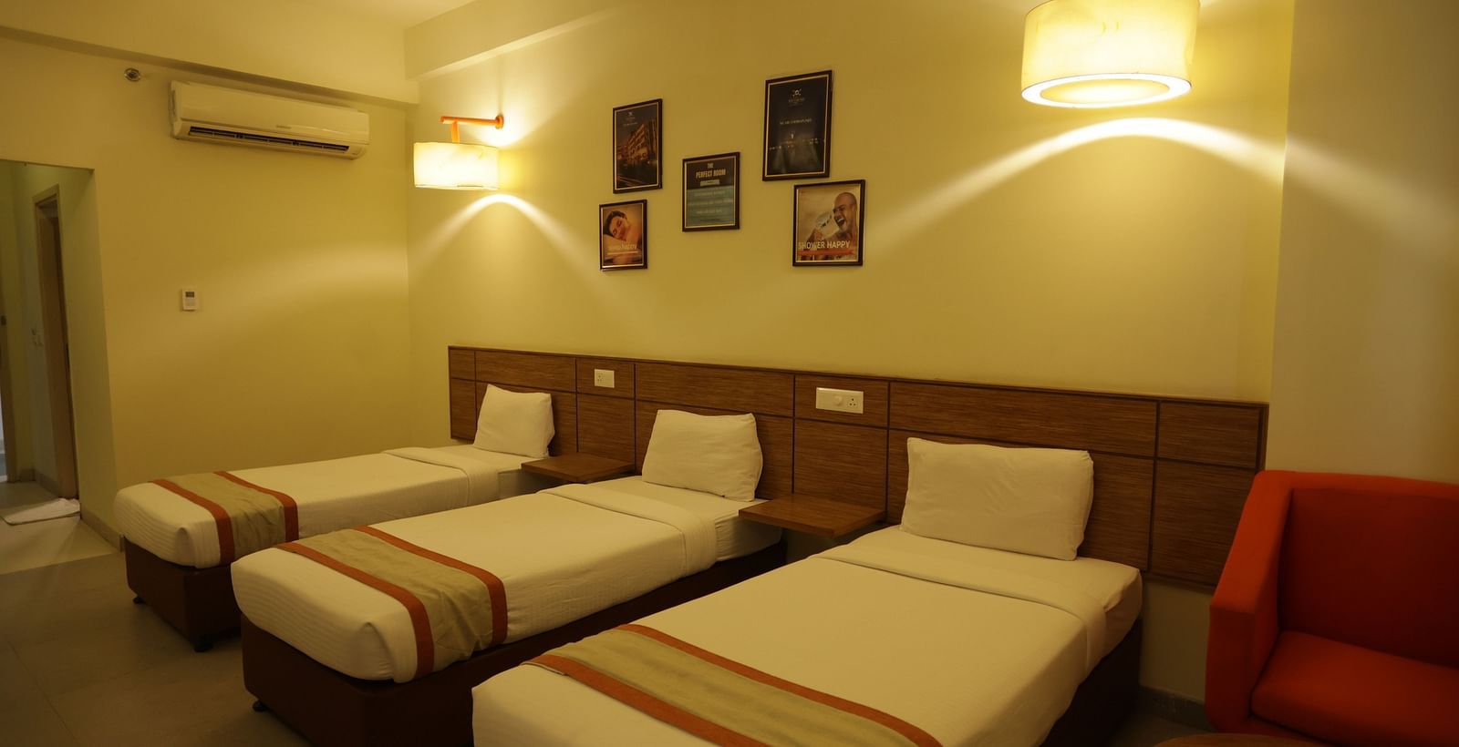 a room with warm lighting featuring three single beds along with a wall mounted air-conditioning - Max Hotel Jabalpur