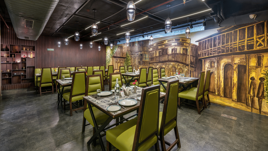 View of a private dining area at Lords Inn Amritsar with green chairs, long dining table, decorative wall murals, and warm ambient lighting.