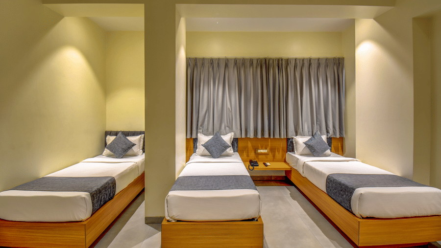 Deluxe Triple Room at VITS Select Nashik Hotels & Resorts featuring 3 single beds arranged next to each other with one separated by a pillar under warm lighting