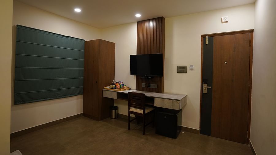 A wide view of the room highlighting the workspace with a desk, a wardrobe, and a mounted TV, providing comfort for both work and relaxation at Hotel Kyzen Smartstays – Smart, Reliable, Kyzen