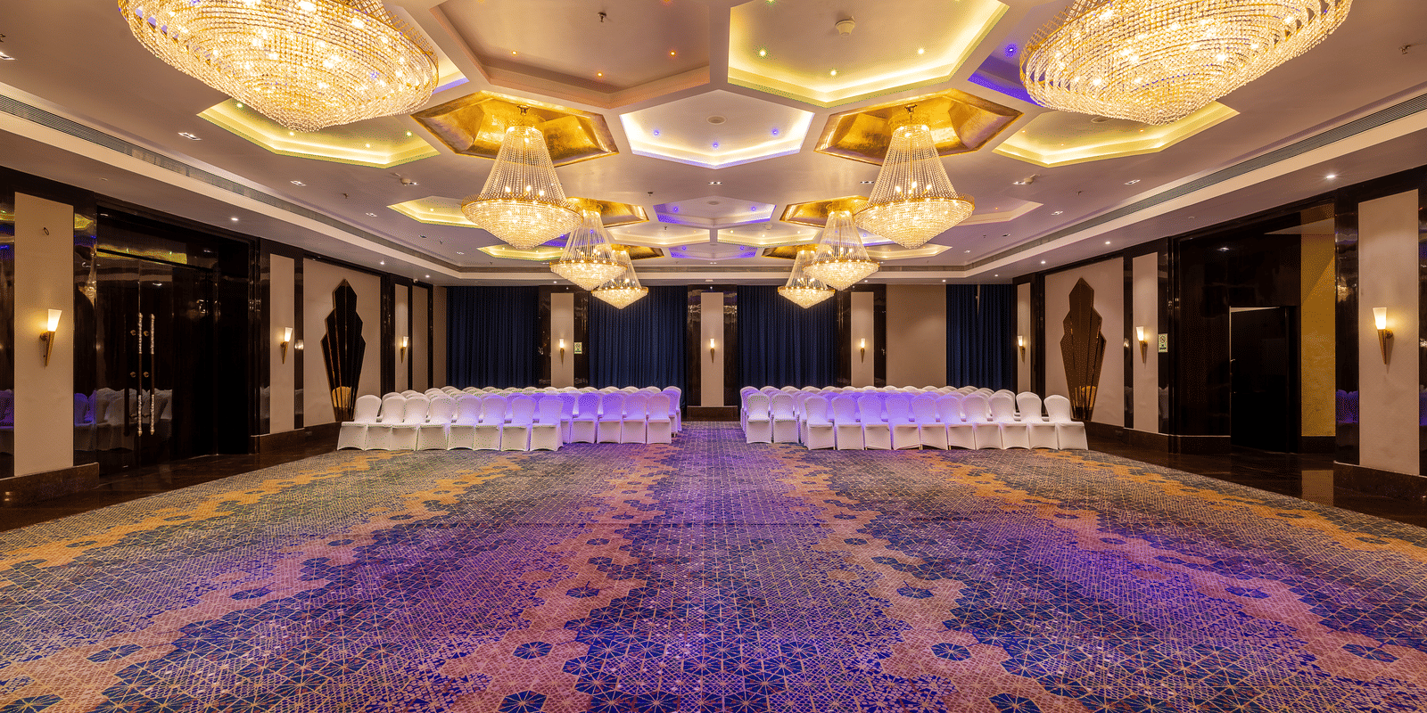 Symmetric view of the large hall featuring multiple tables and chairs, dominated by the elaborate honeycomb chandeliers at Hotel Hukam's Lalit Mahal.