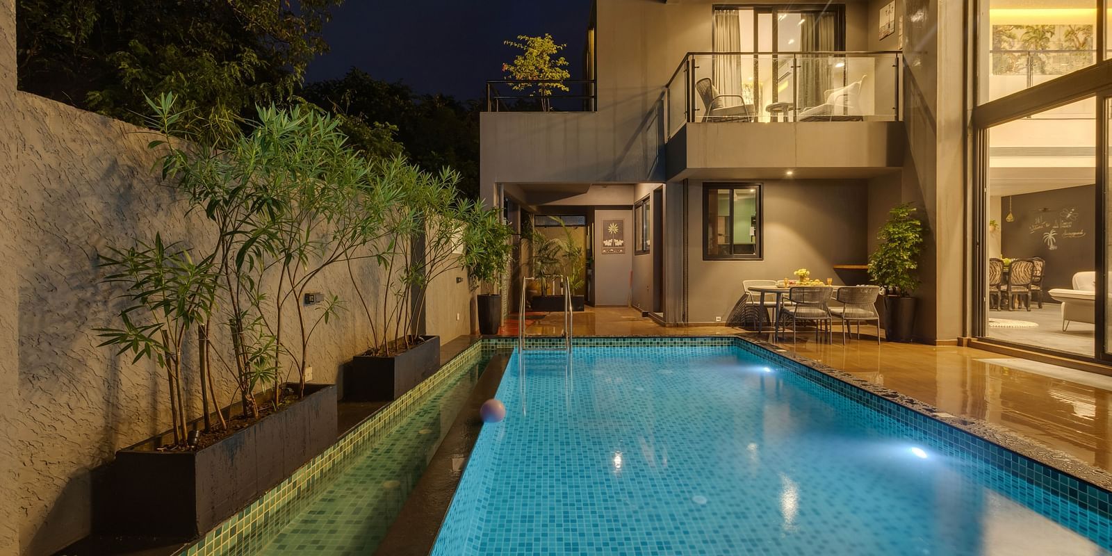 Nighttime view of the pool at Lindsay Manor, with warm light spilling through the glass windows of the living room.
