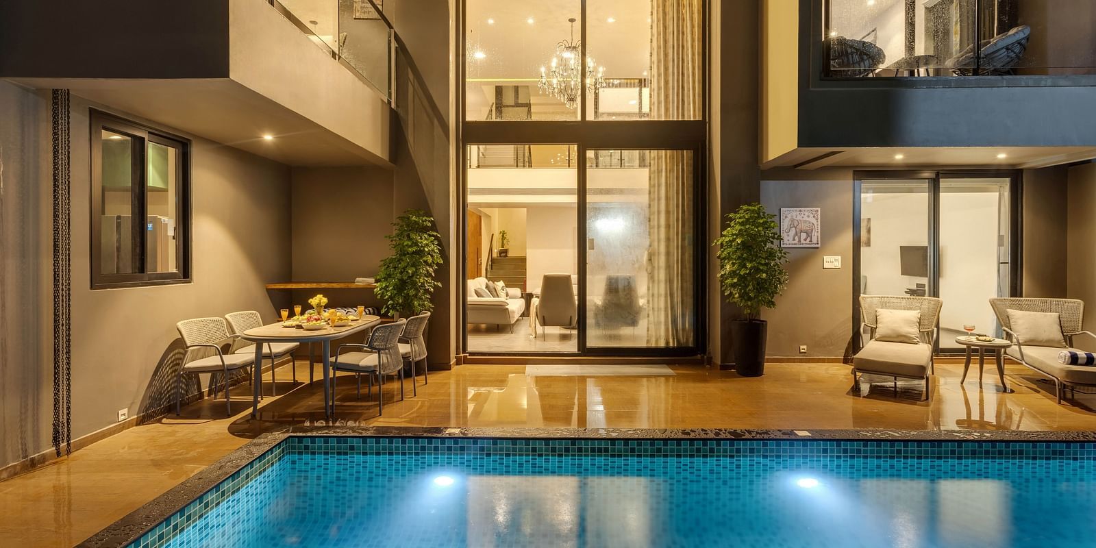 Nighttime pool view at Lindsay Manor, with warm light passing through the living room window and lounge chairs beside the pool.