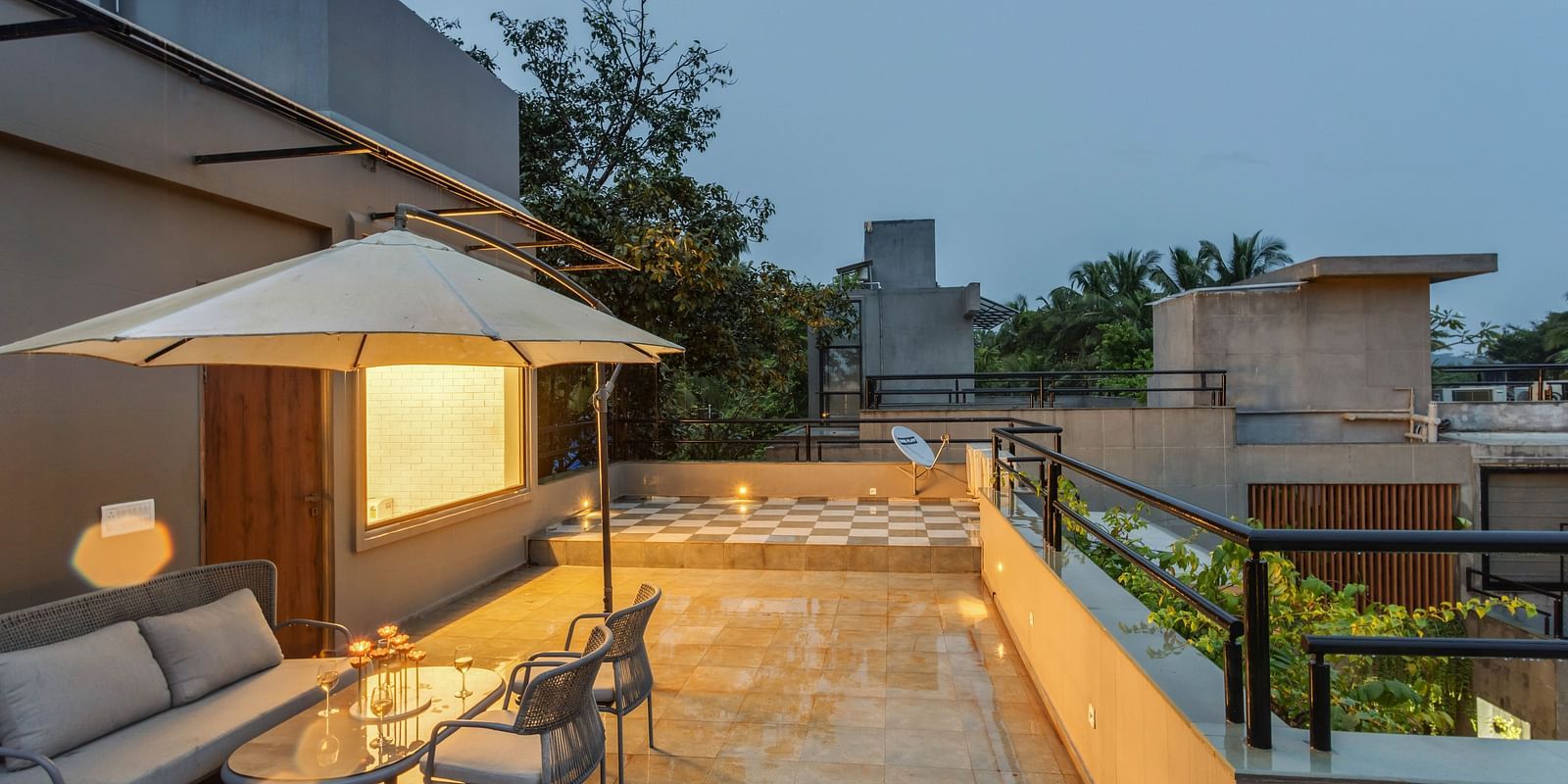Terrace area at Lindsay Manor during the evening, featuring a sofa, tea table, umbrella, and warm light passing through the glass window.