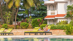 Guests relaxing on sun loungers beside a pool amidst tropical greenery | South Goa Hotel near Beach