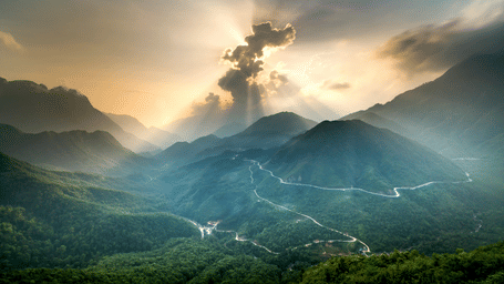 A mountain view with sunrays piercing through the clouds.