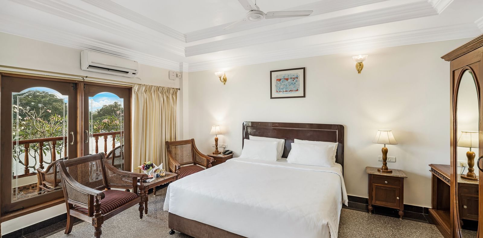 An image of the River Edge Heritage Room featuring a queen size bed, bed side table, lamps, and chairs - GReaT Trails River View Resort Thanjavur By GRT Hotels