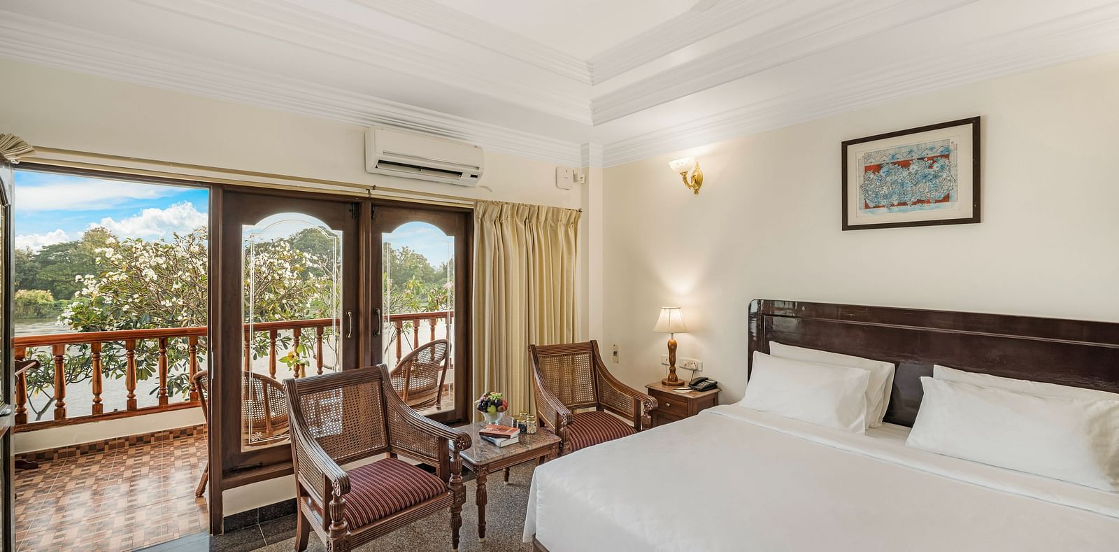 An image of the River Edge Heritage Room featuring a queen size bed, bed side table, lamps, and chairs - GReaT Trails River View Resort Thanjavur By GRT Hotels