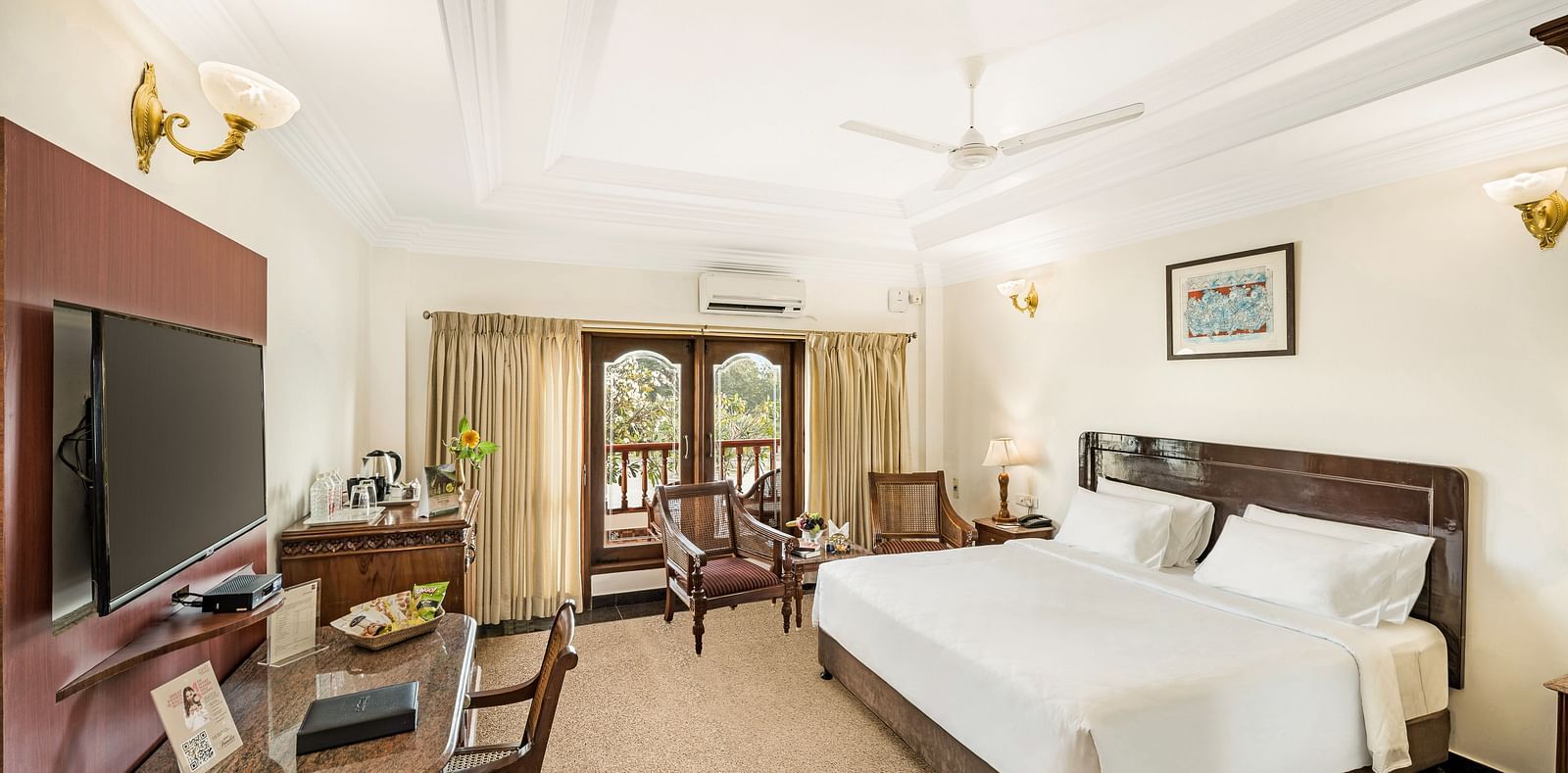 A image of a room with a king size bed, bed side table, flat screen TV, ceiling fan, and a work desk with chair - GReaT Trails River View Resort Thanjavur By GRT Hotels