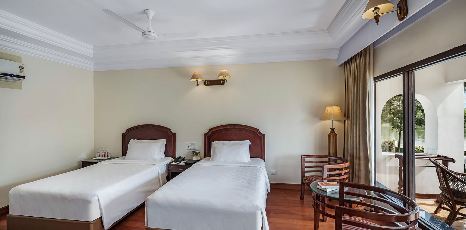 An image of the River View Room With Verandah featuring two single beds, bed side table, lamps, and chairs - GReaT Trails River View Resort Thanjavur By GRT Hotels