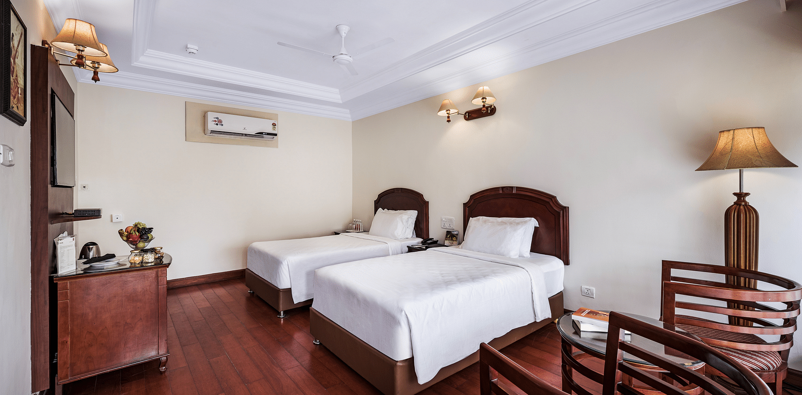 River View Room with balcony featuring two single beds, bed side tables, lamps, flat screen TV, and two chairs - GReaT Trails River View Resort Thanjavur By GRT Hotels