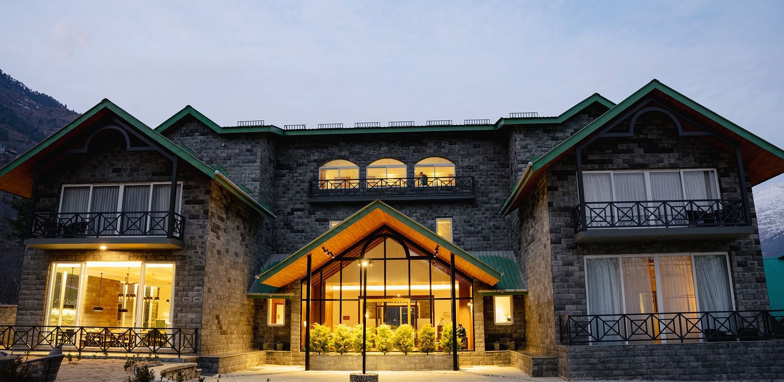 Snow-covered facade with glowing lights at Nivasana Manali during winter dusk.