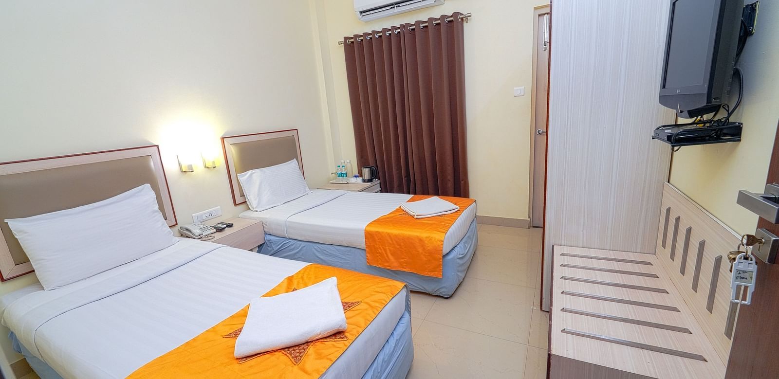 A twin bedroom with light blue bedding, air conditioning, and a wall-mounted TV at Greens Inn - Cozy Accommodations in Ramoji Film City.