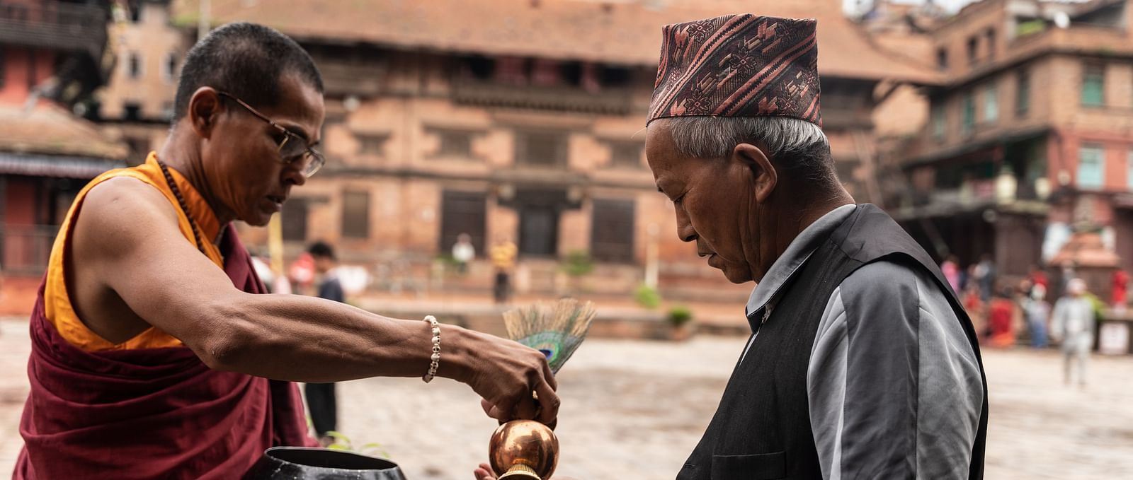 A monk pouring holy water into the palm of an old man