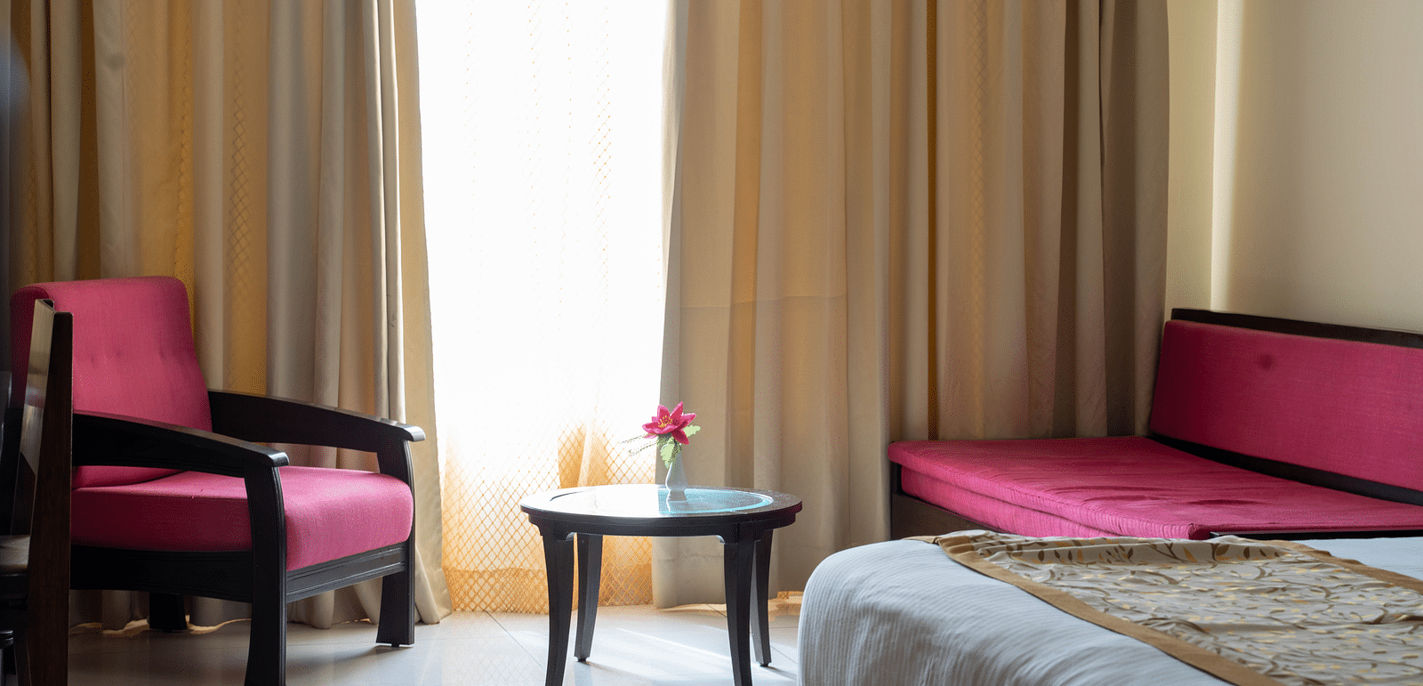 A hotel room with a seating area featuring two armchairs, a coffee table, and large windows with golden curtains - Hotel Udai Median, Udaipur.