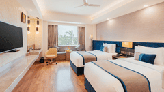 A bedroom with twin beds, padded headboards, workspace unit, and window seating alcove at The Piccadilly Lucknow.