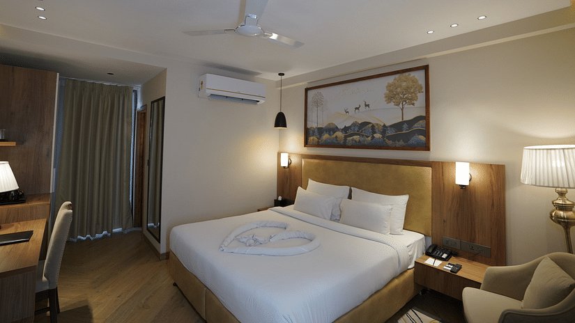 A warm-lit room featuring a king-size bed with a painting above the headboard and an AC mounted next to it at Udman Hotel Chattarpur