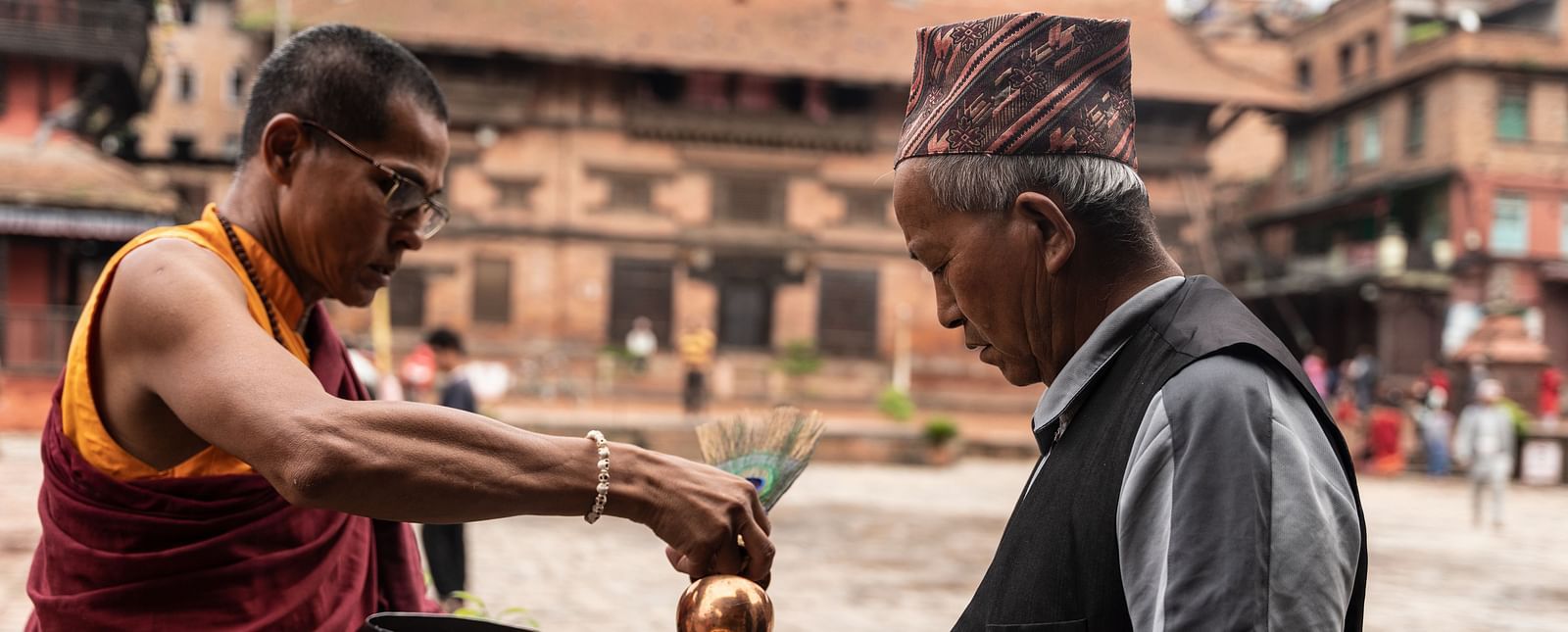 A monk pouring holy water into the palm of an old man